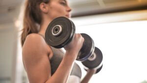 Detail ženy počas cvičenia bicepsového zdvihu s jednoručkami vo fitku.“
